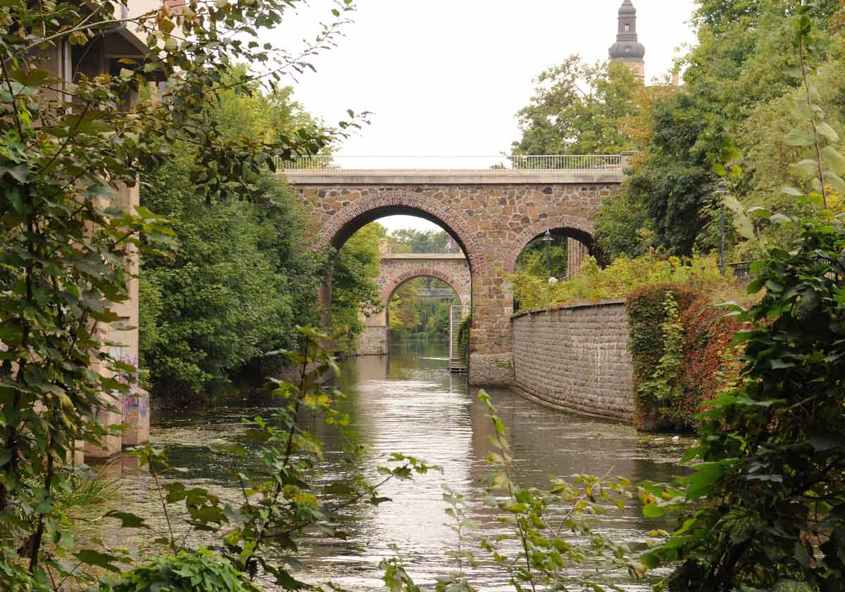 Gebogene Kanalbrücke über einen Wasserweg in Leipzig, idyllisch umgeben von Grün, ein beliebter Ort für Klassenfahrten!